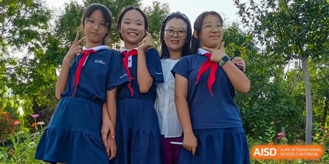 A group of three female students and one female teacher at ZHANGQIU BILINGUAL INTERNATIONAL SCHOOL pose together and smile for a photo outdoors.