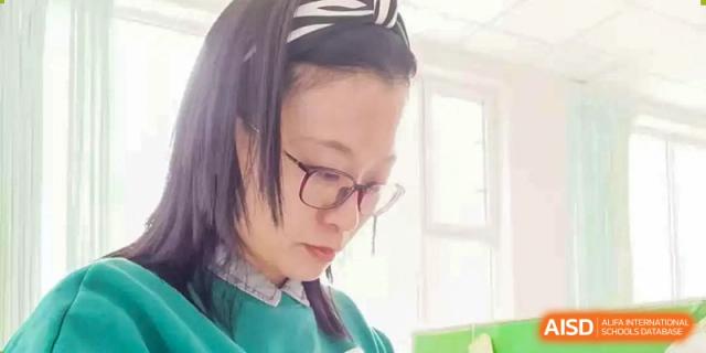 A close-up portrait of a fA close-up portrait of a female teacher or student at ZHANGQIU BILINGUAL INTERNATIONAL SCHOOL wearing glasses and looking down at her work.