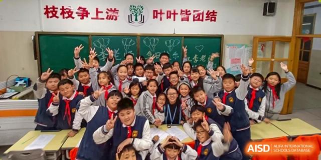 A large group of happy students at ZHANGQIU BILINGUAL INTERNATIONAL SCHOOL smile for a photo in front of a green chalkboard with Chinese writing.