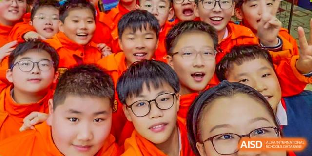 A close-up of a group of excited male students from ZHANGQIU BILINGUAL INTERNATIONAL SCHOOL smiling brightly for a photo.