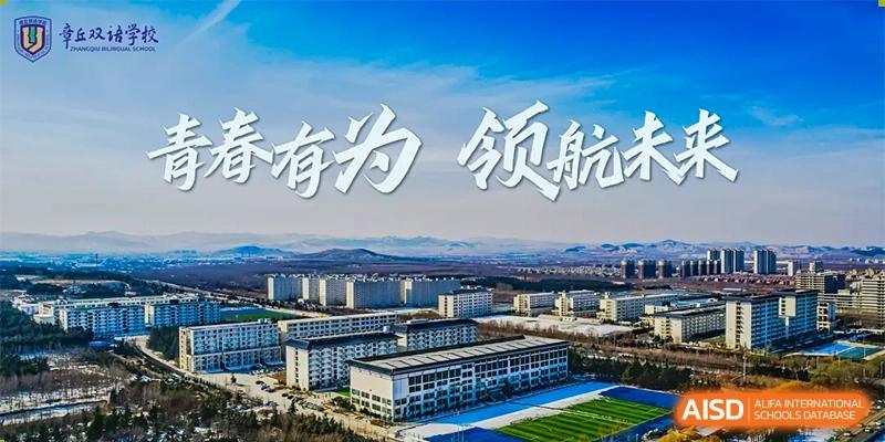 An aerial or wide-shot view of the modern campus buildings and grounds of ZHANGQIU BILINGUAL INTERNATIONAL SCHOOL with a Chinese slogan in the sky.