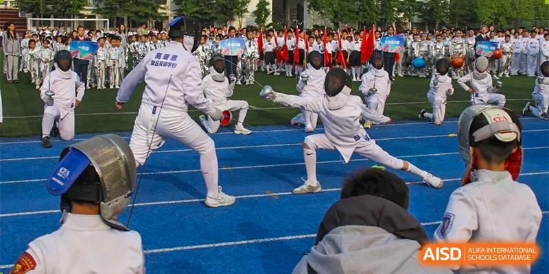 Students at ZHANGQIU BILINGUAL INTERNATIONAL SCHOOL  participate in a fencing competition on a blue track during a sports event.