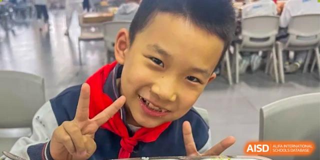 A close-up portrait of a smiling male student at ZHANGQIU BILINGUAL INTERNATIONAL SCHOOL holding up a V-sign.