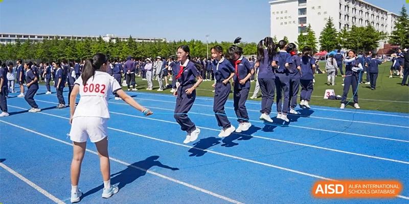 A group of female students at ZHANGQIU BILINGUAL INTERNATIONAL SCHOOL participate in a synchronized jump-roping activity on a blue track.