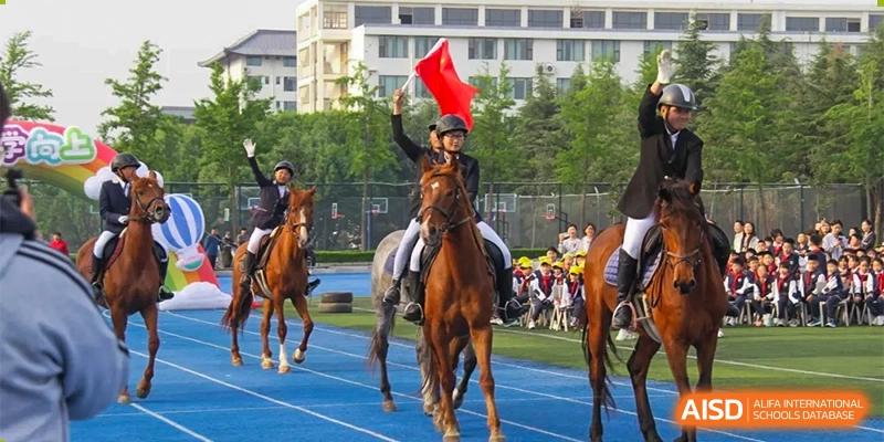 A student from ZHANGQIU BILINGUAL INTERNATIONAL SCHOOL rides a horse while holding a red flag during an outdoor school parade or ceremony.