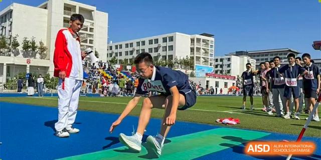 A male student at ZHANGQIU BILINGUAL INTERNATIONAL SCHOOL performs a long jump or high-intensity jump during a sports day competition.
