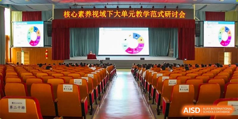 An auditorium or lecture hall at ZHANGQIU BILINGUAL INTERNATIONAL SCHOOL shows a large screen with a pie chart presentation on stage.