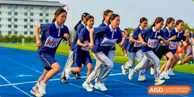 A group of female students from ZHANGQIU BILINGUAL INTERNATIONAL SCHOOL runs a race on a blue track during a sports competition.