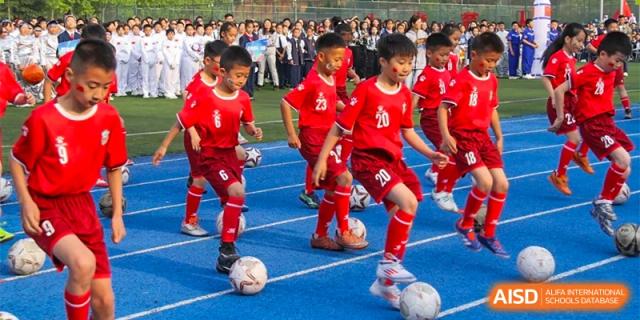 A group of young male students from ZHANGQIU BILINGUAL INTERNATIONAL SCHOOL in red uniforms plays football (soccer).