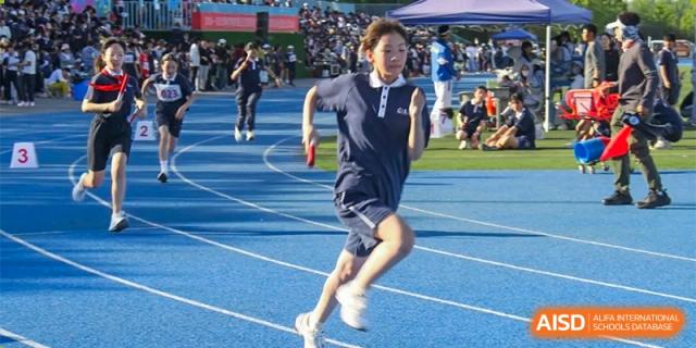 A female student from ZHANGQIU BILINGUAL INTERNATIONAL SCHOOL runs on a blue track during an athletics event.