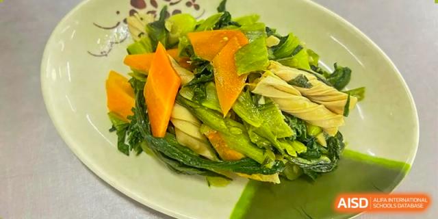 A plate of bright green stir-fried leafy vegetables and sliced carrots served as a healthy side dish at ZHANGQIU BILINGUAL INTERNATIONAL SCHOOL