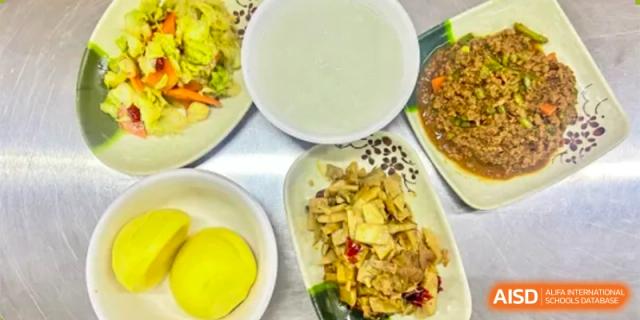 A variety of dishes, including meat, vegetables, and a bowl of white soup or porridge, part of a meal served at ZHANGQIU BILINGUAL SCHOOL.