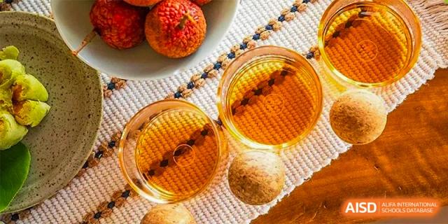 Two glasses of golden-colored beverage, possibly iced tea or juice, with lychee fruit on a checkered mat at ZHANGQIU BILINGUAL SCHOOL.