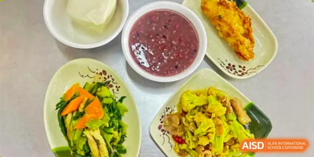 A high-angle view of a bowl of dark red bean or purple rice soup surrounded by other healthy food dishes served at ZHANGQIU BILINGUAL INTERNATIONAL SCHOOL.
