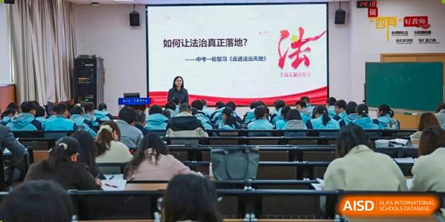 A teacher from Nanjing Dongshan Foreign Language School International Department is giving a presentation on a stage to a group of students.