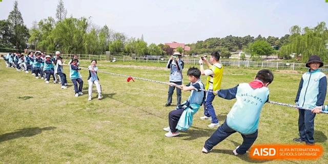 A group of students from Nanjing Dongshan Foreign Language School International Department walking on a grassy field with a teacher.