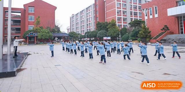 A large group of students from Nanjing Dongshan Foreign Language School International Department wearing white shirts and blue pants, walking in formation outdoors.