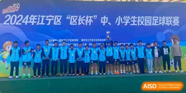 Students from Nanjing Dongshan Foreign Language School International Department are standing on a stage with a banner that reads "区'区长杯'中、小学".