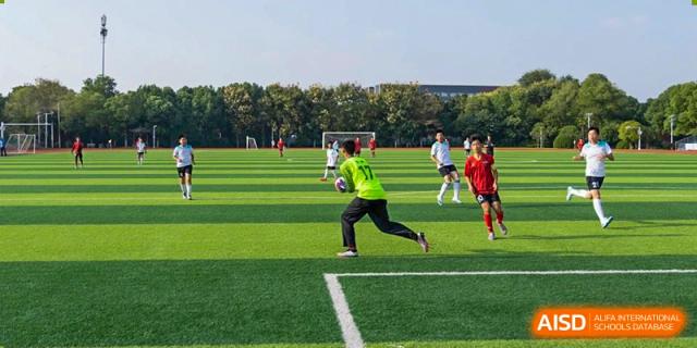 A soccer player from Nanjing Dongshan Foreign Language School International Department is kicking a ball on a green field.