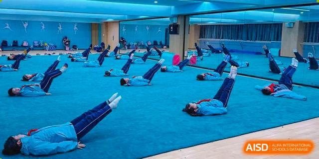 Students from Nanjing Dongshan Foreign Language School International Department are doing yoga or stretching on mats in a gym.