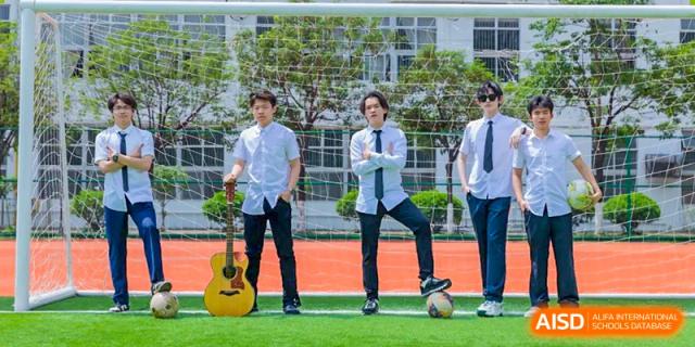 Students from Nanning No.2 High School International Division are smiling and posing with a soccer ball on a field.
