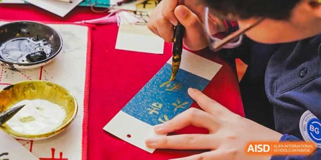 A BASIS International & Bilingual Schools Chengdu student using a pen to write on a red notebook or paper.