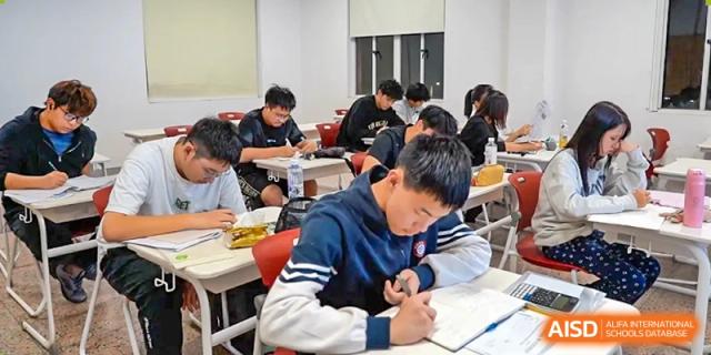 AcaBridge Academy students intensely focused on writing notes or working on assignments at their desks in a busy classroom.