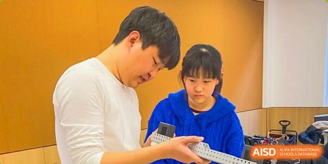 An AcaBridge Academy teacher and a female student working together on a hands-on project, holding a metal component.