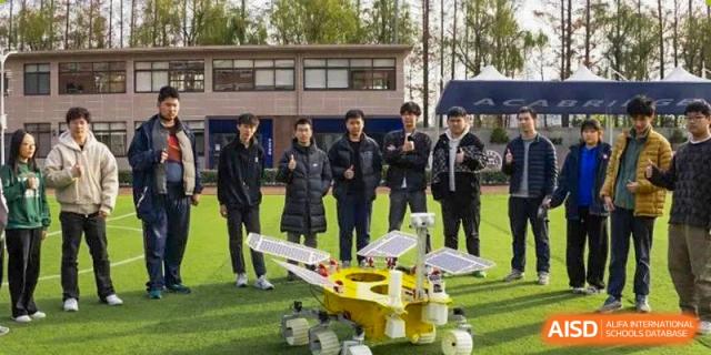 AcaBridge Academy students standing outdoors around a small, yellow robotic rover with solar panels on a sports field.