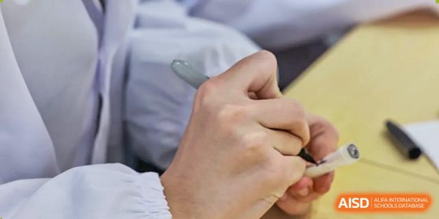 A close-up shot of an AcaBridge Academy student's hands writing notes or data with a pen during a lab or field observation.