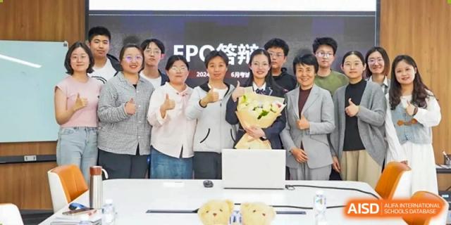 AcaBridge Academy students and faculty celebrating a success, holding a bouquet of flowers and giving thumbs up behind a laptop.