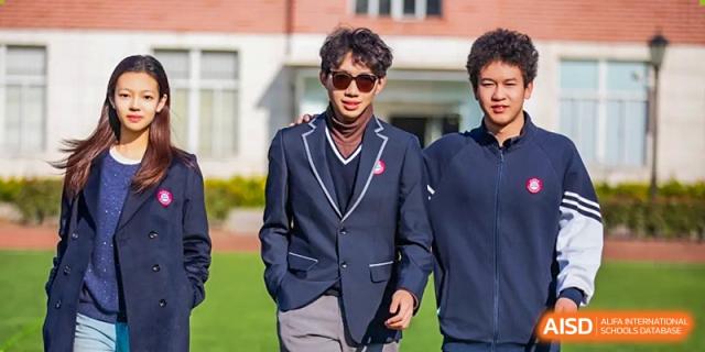 An AcaBridge Academy student wearing a dark suit jacket, sunglasses, and a red necktie, posing outdoors on the school grounds.