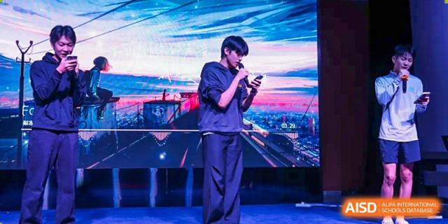 AcaBridge Academy student on stage holding a microphone and phone, dressed in a dark hoodie and pants, performing in front of a bright, colorful background.
