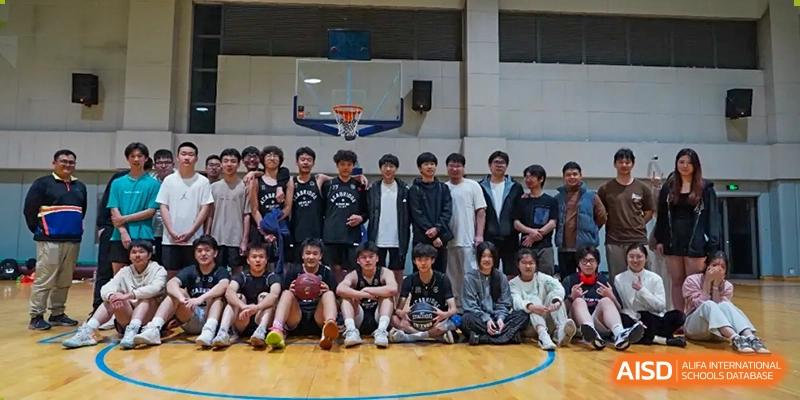 A group of AcaBridge Academy students posing for a team photo on a basketball court, sitting and standing together in front of a hoop and backboard.