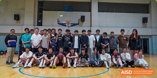A group of AcaBridge Academy students posing for a team photo on a basketball court, sitting and standing together in front of a hoop and backboard.