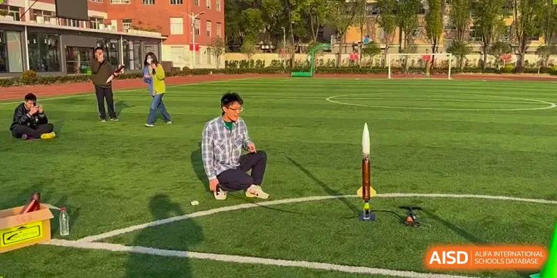 An AcaBridge Academy student crouching on a sports field next to a small, homemade or model rocket standing upright.