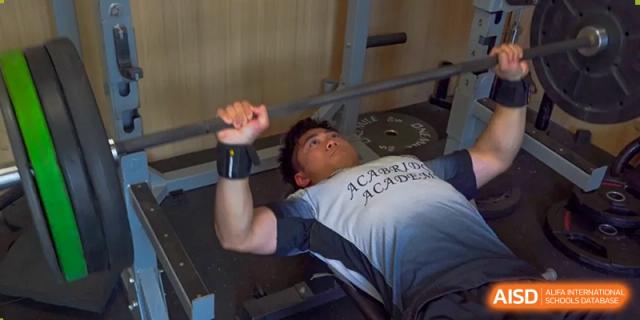 An AcaBridge Academy student working out in a gym, wearing a shirt with the school's name on it while lifting weights.