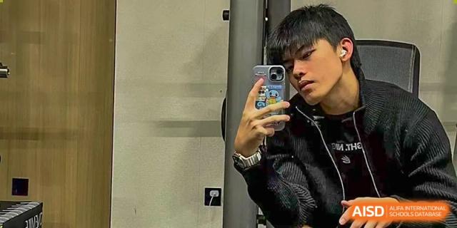 An AcaBridge Academy student taking a mirror selfie while holding a phone and wearing a dark jacket.
