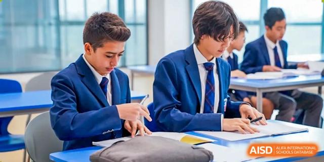 Merchiston International School Shenzhen students in their navy blue blazers are focused on writing and working together at a classroom desk.