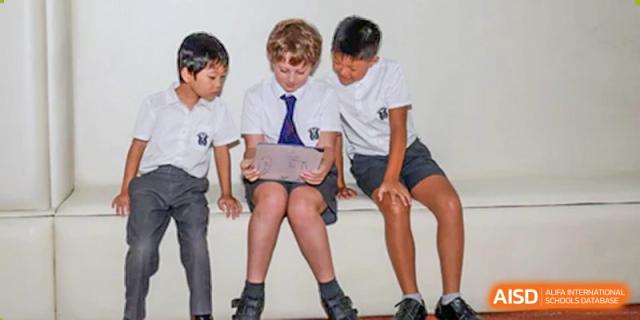 A diverse group of Merchiston International School Shenzhen primary students sitting together, collaborating and reading from a digital tablet.