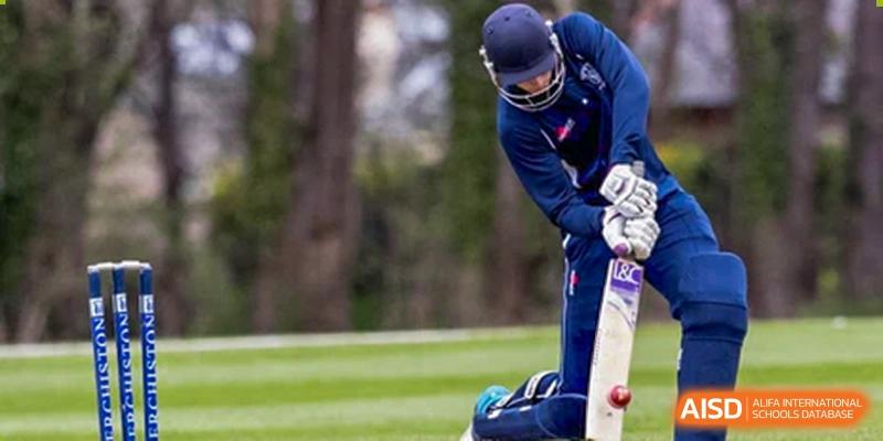 A Merchiston International School Shenzhen student wearing a helmet and pads, playing cricket outdoors with a bat and ball.