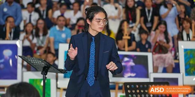 A confident Merchiston International School Shenzhen student presenting or speaking on stage to an audience at a school event.