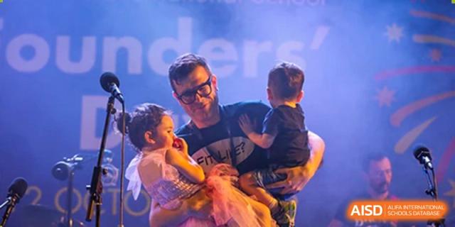 A father holding his young children backstage or after a performance at a Merchiston International School Shenzhen event.