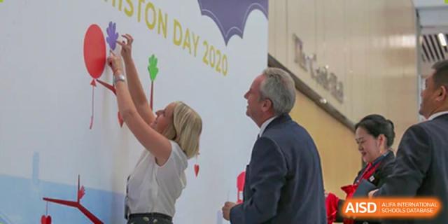 Adults, including school staff, celebrating or interacting near a banner for a Merchiston International School Shenzhen community day.