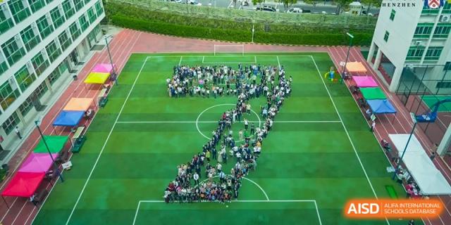 Merchiston International School Shenzhen students forming a large number or symbol on the green sports field as viewed from above.