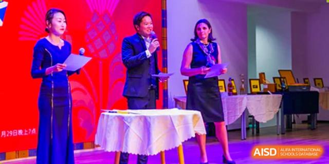 Two teachers or hosts presenting awards or speaking on stage during a formal Merchiston International School Shenzhen event.