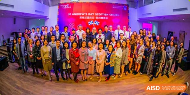 A large group of staff, parents, and community members posing in front of a banner for the St. Andrew's Day Scottish Celebration at Merchiston International School Shenzhen.
