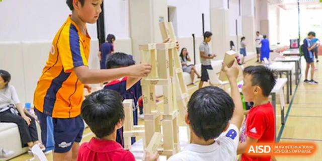 Merchiston International School Shenzhen students collaborating to build a tall structure using wooden blocks during a creative or STEM activity.