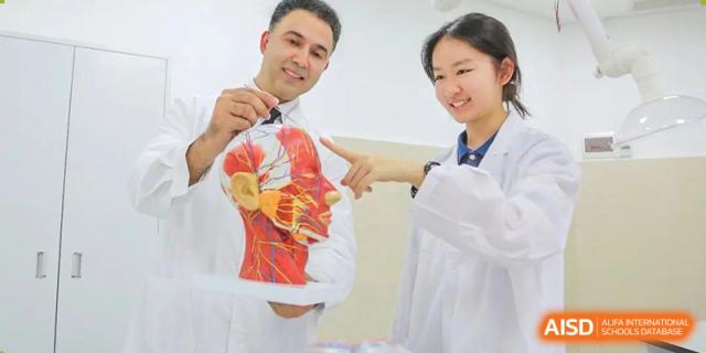 A teacher from Guangdong Country Garden School holds up a t-shirt with a drawing on it while talking to two students.