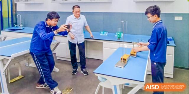 A teacher from Guangdong Country Garden School stands in a science lab with students, pointing to a lab setup.
